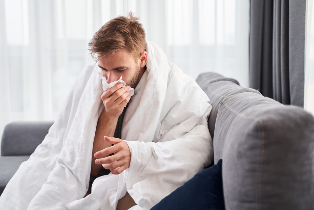 sick man with blanket over shoulders and blowing nose