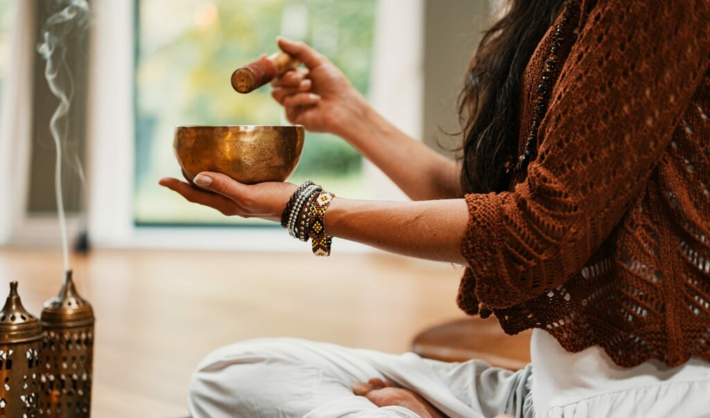 Woman sits cross-legged with a singing bowl and incense sticks