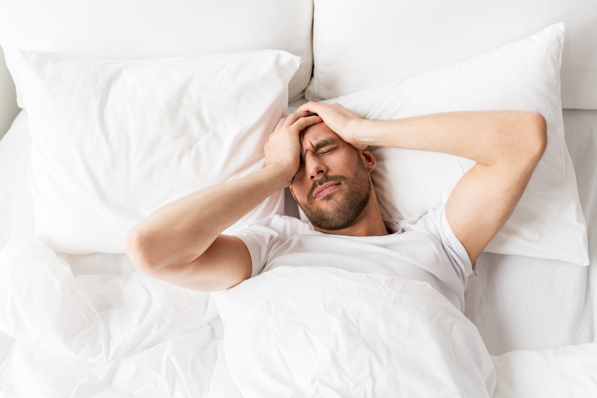 Ein Mann liegt im Bett und hält sich den Kopf wegen Kopfschmerzen