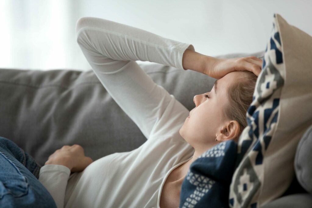 Frau liegt auf Couch und hält sich vor Kopfschmerzen den Kopf