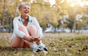 Aeltere Frau sitzt lachend auf einer Wiese