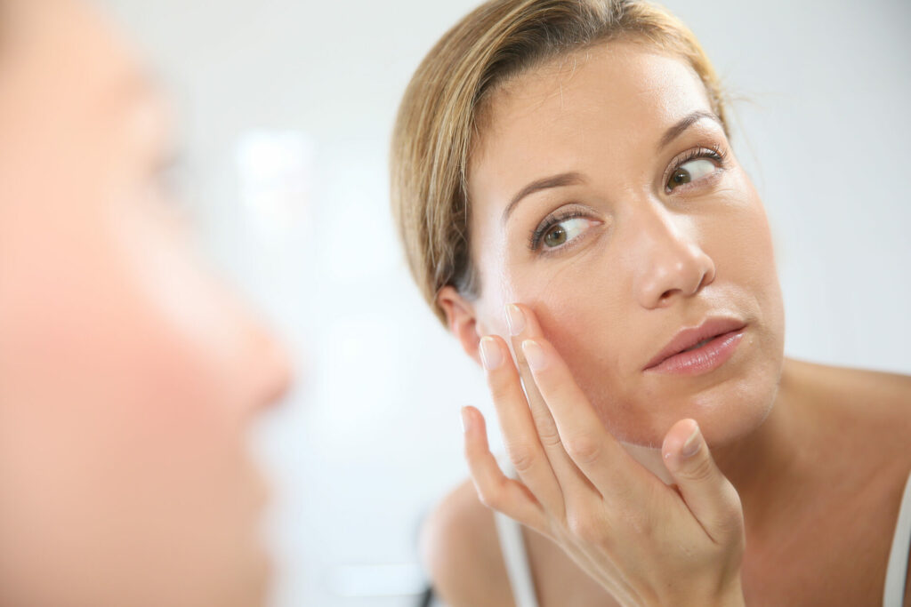 Woman looks at herself in the mirror and strokes her cheek with her finger.