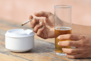 Person holds a cigarette in one hand and a glass of beer in the other