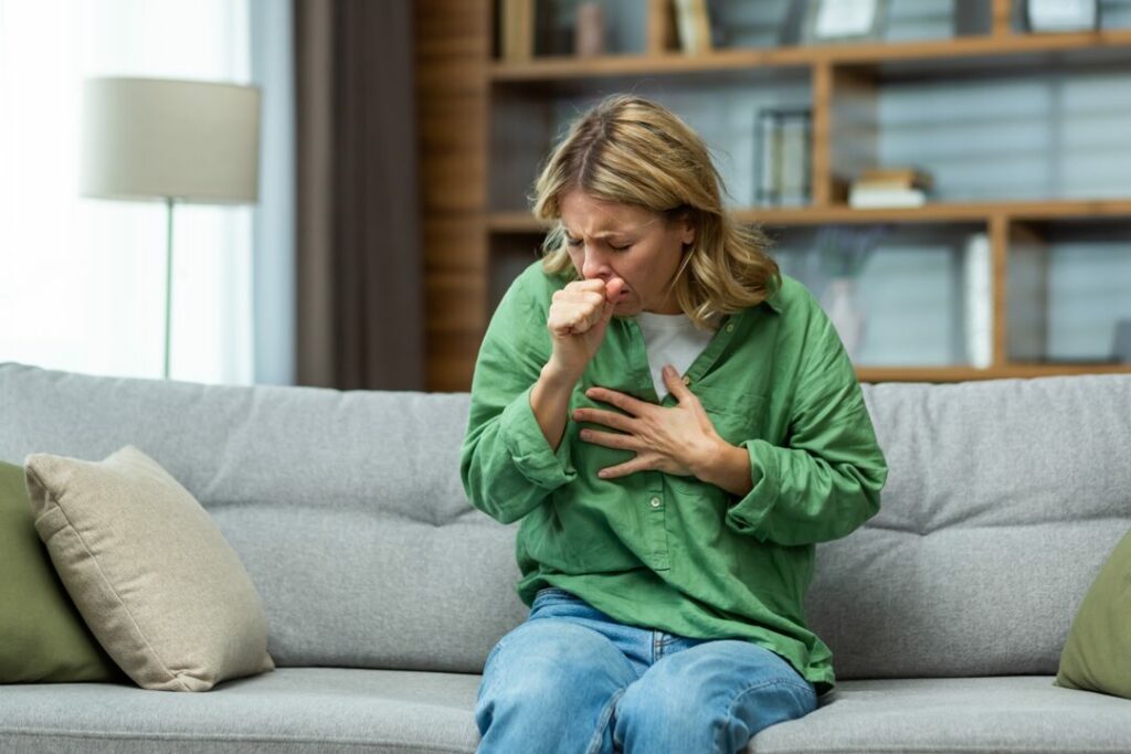 Woman sits on couch and has an asthma cough attack