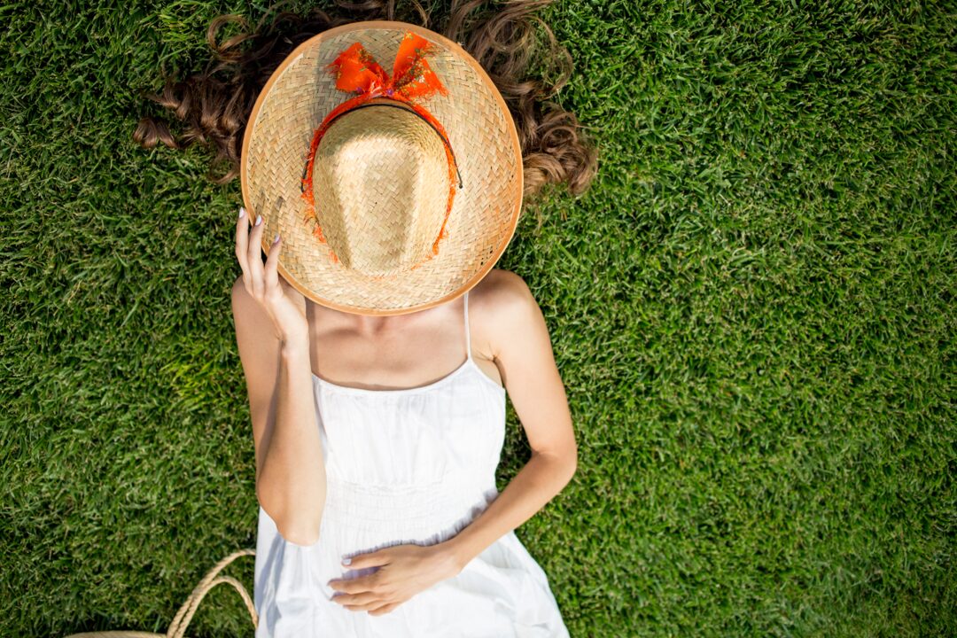 Woman lying on a lawn with a hat over her face and sunbathing. Avoid sun allergy